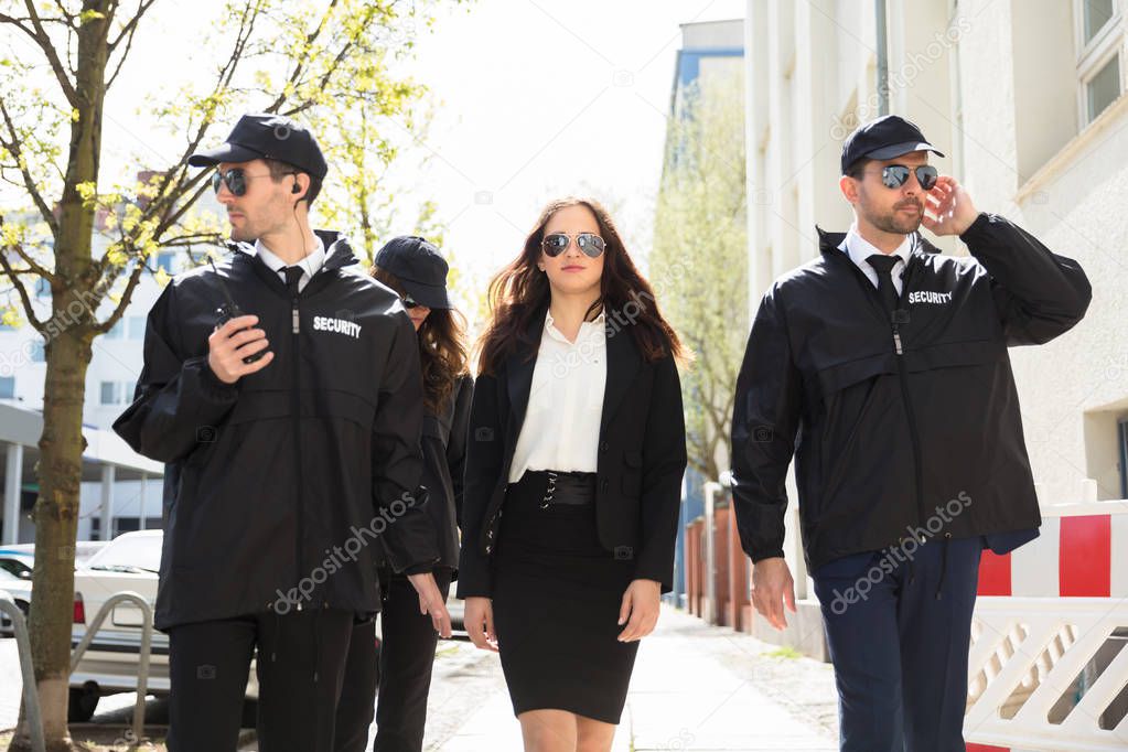 Portrait Of Young Female Celebrity With Bodyguards Walking On Sidewalk