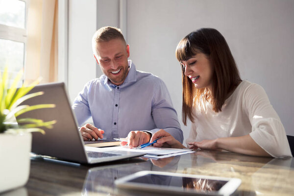Two Happy Businesspeople Working On Document With Laptop On Desk