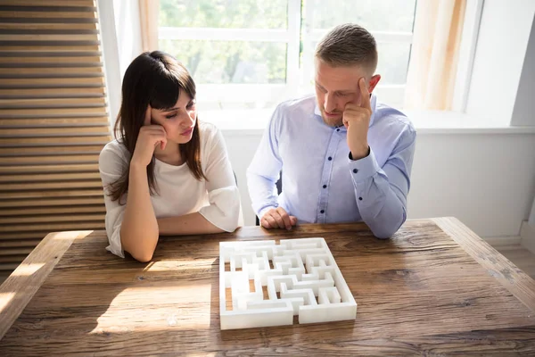 Two Contemplated Young Businesspeople Solving Maze Puzzle Wooden Desk — Stock Photo, Image