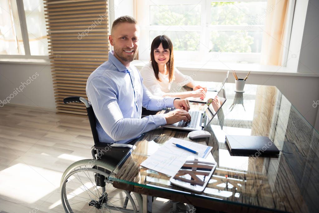 Portrait Of Smiling Disabled Businessman With His Colleague Working On Laptop