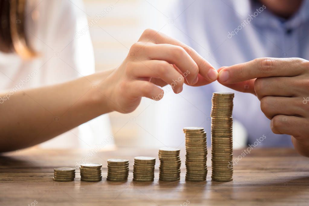 Couple Stacking Golden Coins Over Wooden Desk