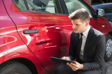 Sigortacı zarar görmüş kırmızı araba yakınındaki sigorta formu doldurma