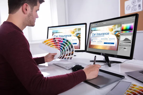 オフィス内のコンピューターに取り組んでいるカラフルな色見本を保持している若い男性デザイナーの側面図 — ストック写真