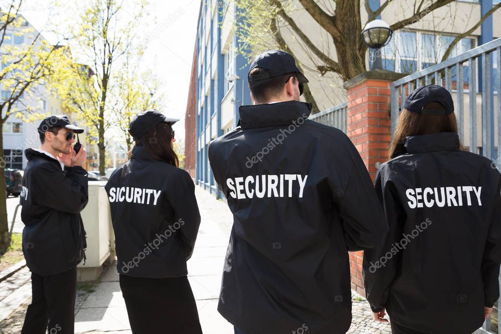 Rear View Of Security Guards In Black Uniform Standing Outside Building