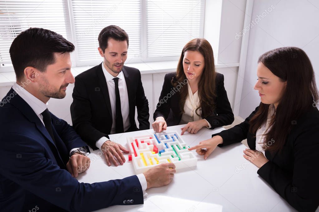 Young Businesspeople Holding Multi Colored Arrow Solving Maze On Desk At Workplace