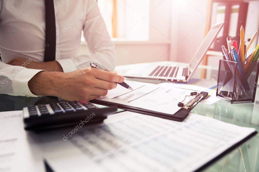 Close-up Of A Businessman Checking Invoice Over Desk