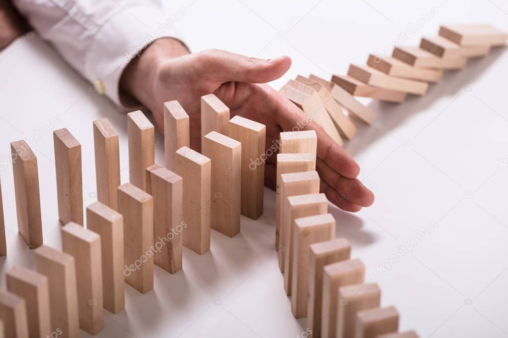 Close-up Of A Businessperson's Hand Stopping Wooden Blocks From Falling On White Background