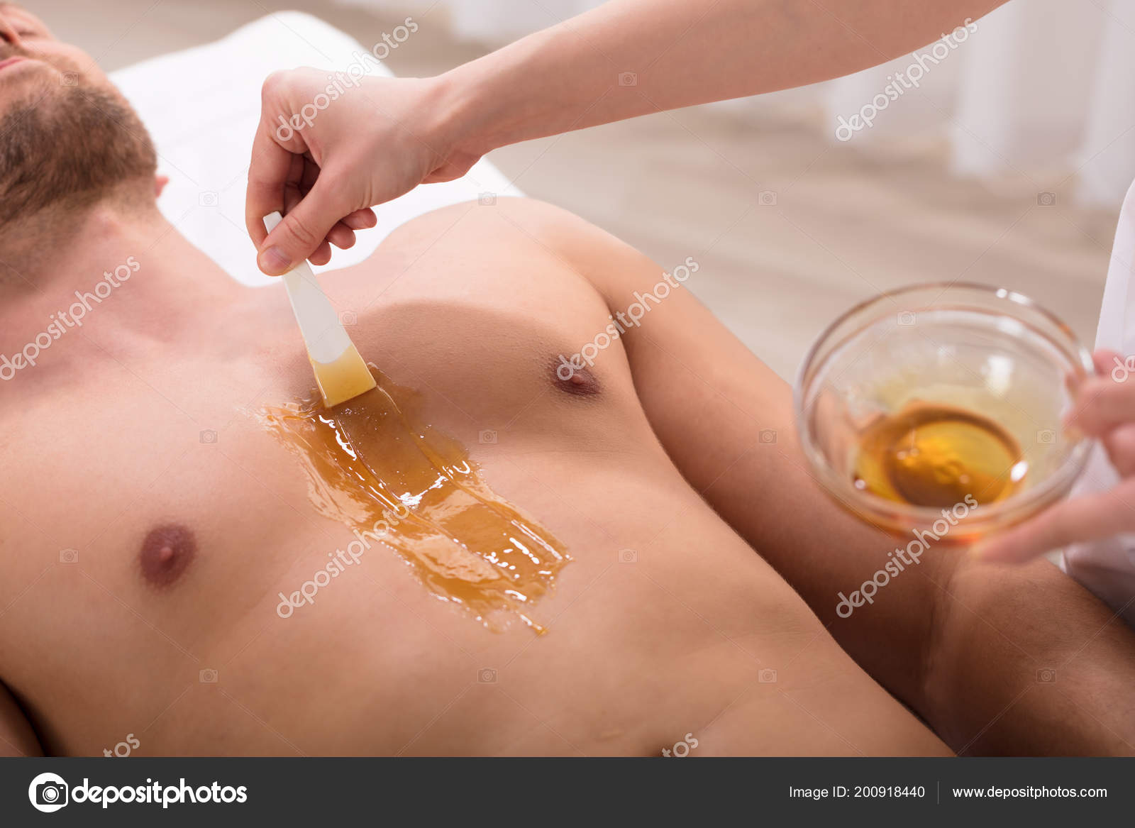 Close-up Of Therapist Hand Applying Wax On Relaxed Young Man's
