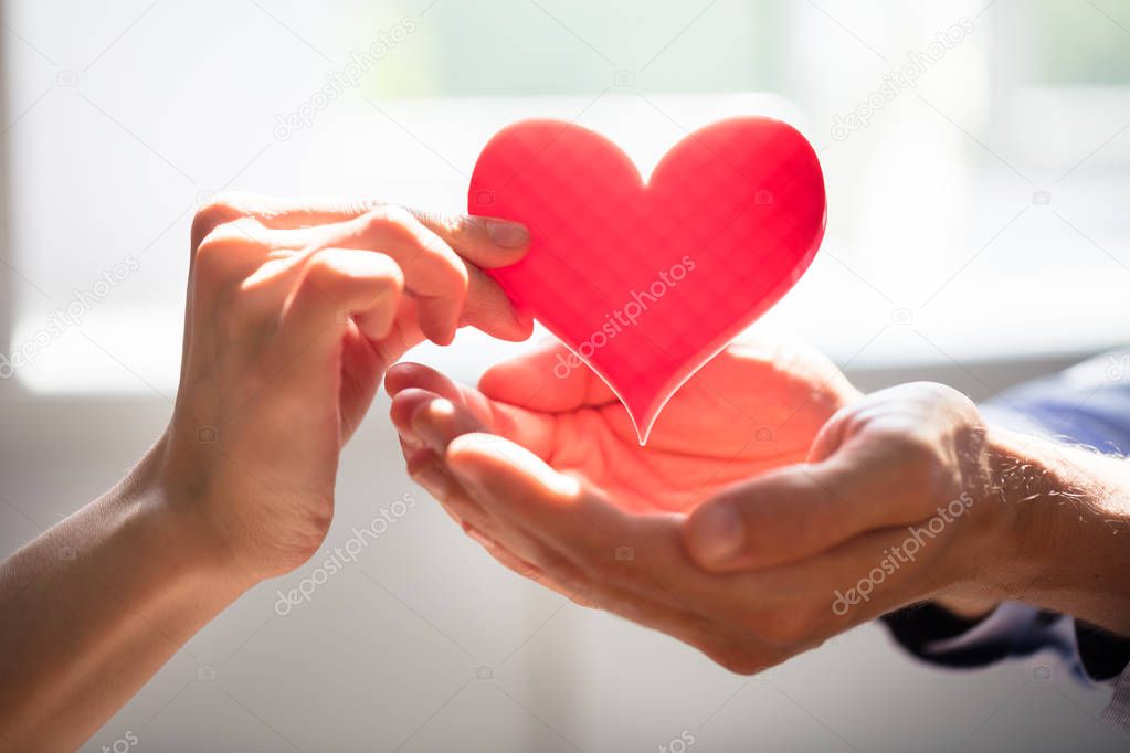 Close-up Of Woman Giving Red Heart On Man's Hand