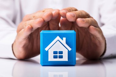 İnsan eli ile yansıtıcı masa üzerinde ev simgesini mavi küp blok korumak