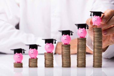 Piggybank mezuniyet şapka ile yığılmış sikkelerinde yerleştirerek bir birinin elini Close-up