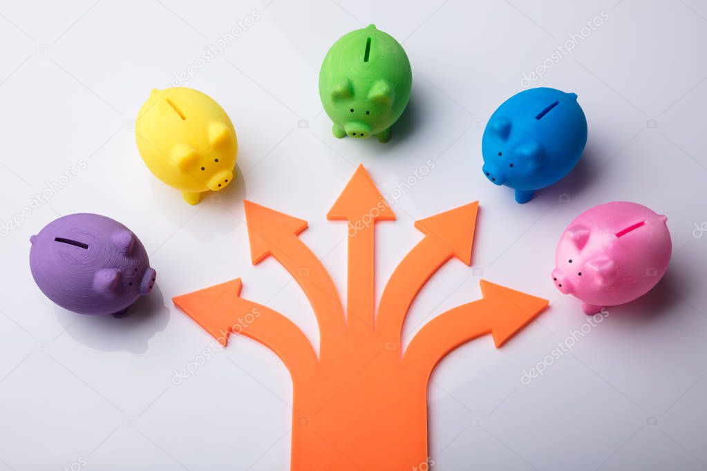 Various Arrow Symbols Showing Direction Towards Colorful Piggybanks Over White Background