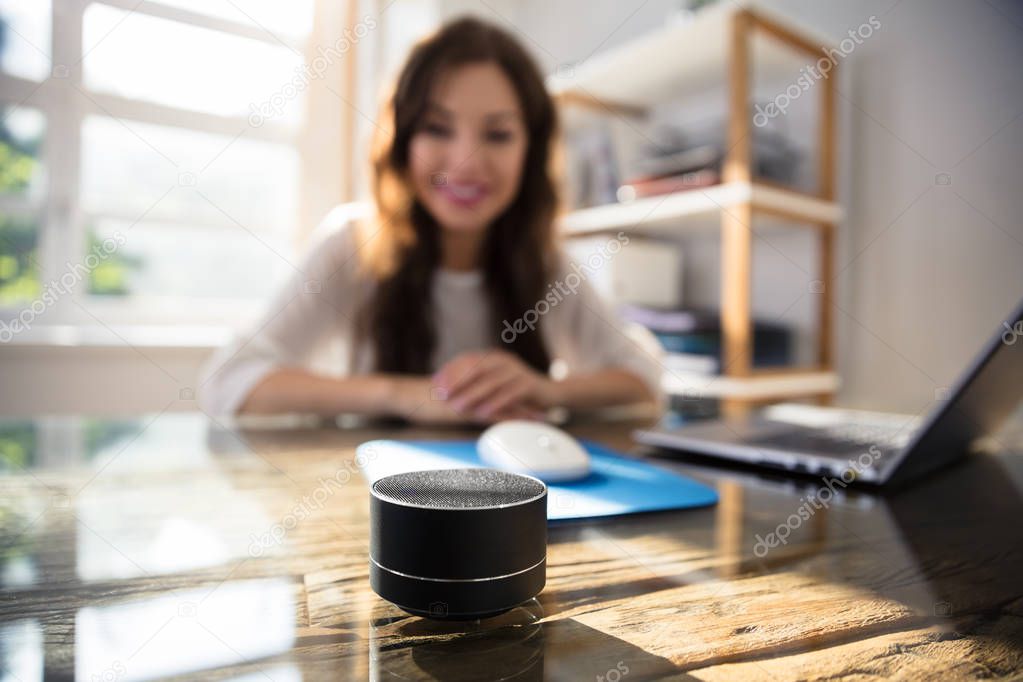 Close-up Of Wireless Speaker In Front Of Businesswoman Listening To Music