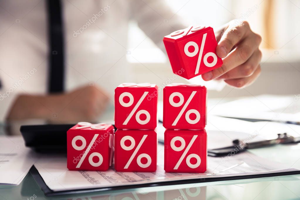 Close-up Of A Businessperson's Hand Building Cubic Blocks With Percentage Symbols Over Desk