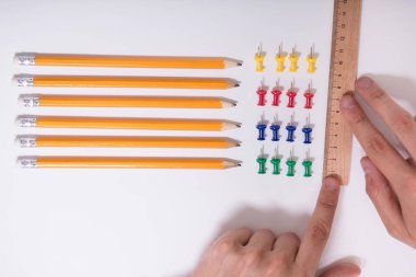 A Person's Hand Arranging Pencils And Multi Colored Pushpins In A Row On White Background clipart