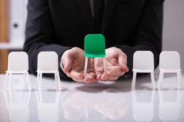 Beyaz sandalyeler arasında yeşil koltuk sunan işadamı