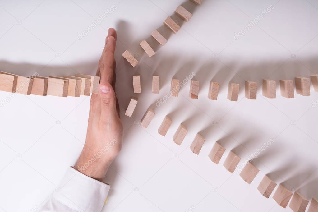 Close-up Of A Businessperson's Hand Stopping Wooden Blocks From Falling On White Background