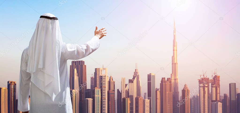 Rear View Of A Arabic Man Outstretching His Hand At Modern Buildings In Dubai