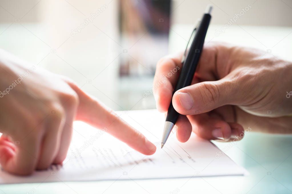 Close-up Of Businessperson's Hand Assisting Employee While Signing Document
