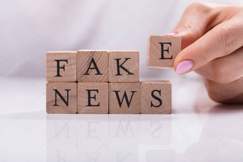 Businesswoman's Hand Building Blocks With Fake News Word Over Desk