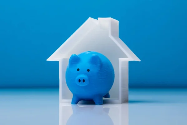 Крупный План Piggybank Модели Дома Перед Синим Фоном — стоковое фото