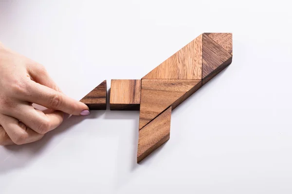 Close-up Of A Woman's Hand Making Rocket With Wooden Tangram Puzzle On White Background