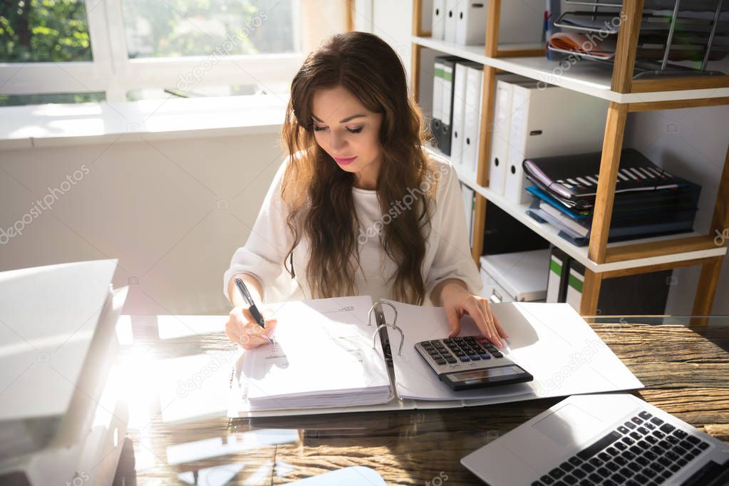 Young Businesswoman Calculating Bill With Calculator In Office