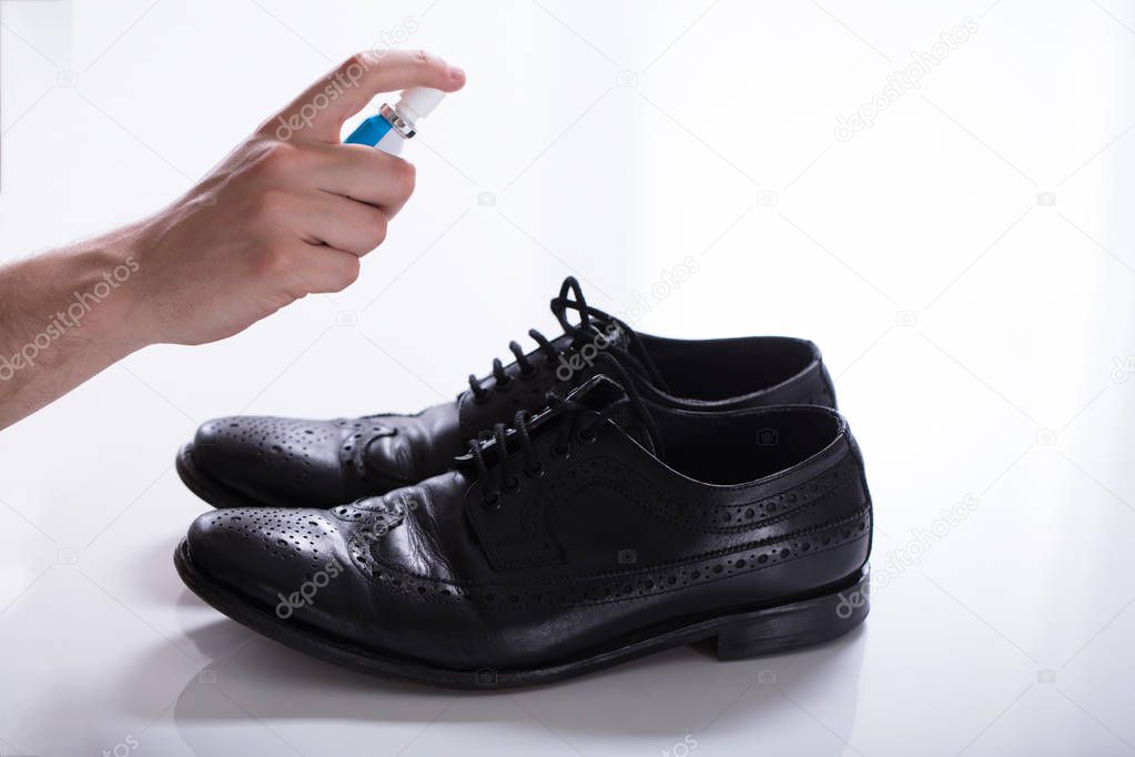 Man's Hand Spreading Deodorant On Smelly Shoes Against White Background