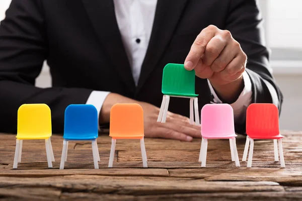 Mano Del Empresario Recogiendo Silla Verde Entre Otros Escritorio Madera — Foto de Stock