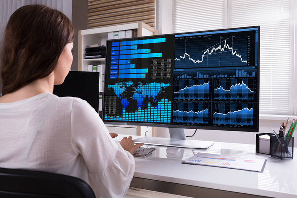 Женский брокер фондового рынка анализирует графики на компьютере на рабочем месте
