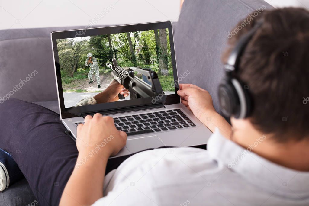 Man wearing headphone playing shooting game on laptop