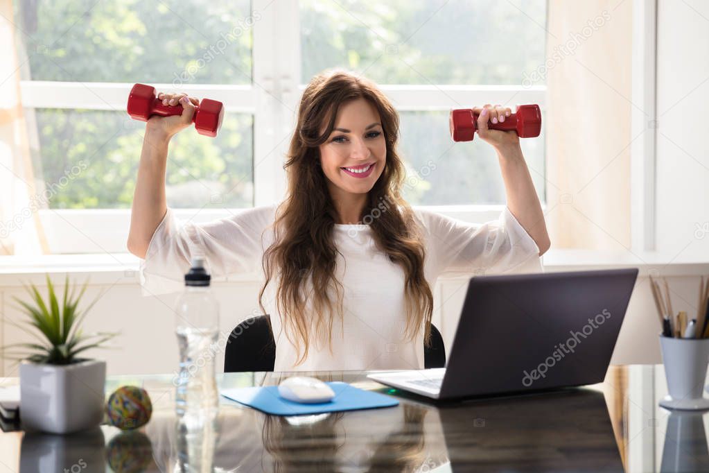 Smiling Young Businesswoman Exercising With Red Dumbbells