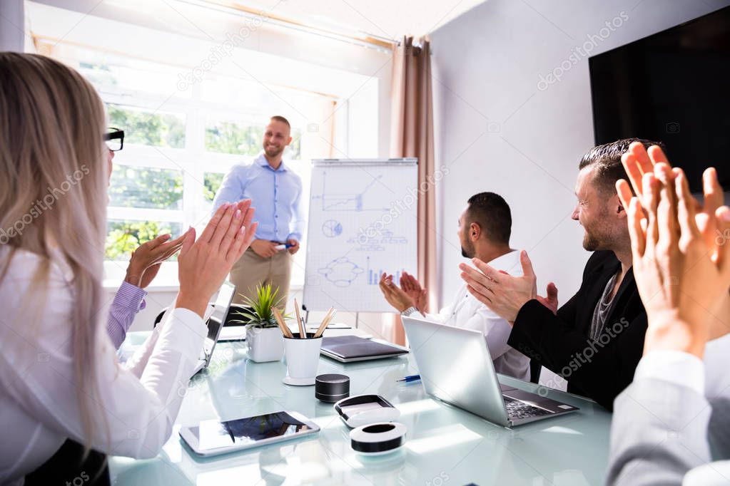 Businesspeople Applauding Their Smiling Male Colleague After Presentation At Workplace