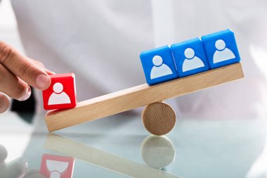 Person showing unbalance between single red block and blue blocks with human figures on seesaw clipart