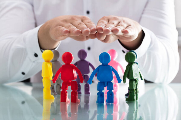 Рука человека защищает разноцветные человеческие фигуры, образующие круг
