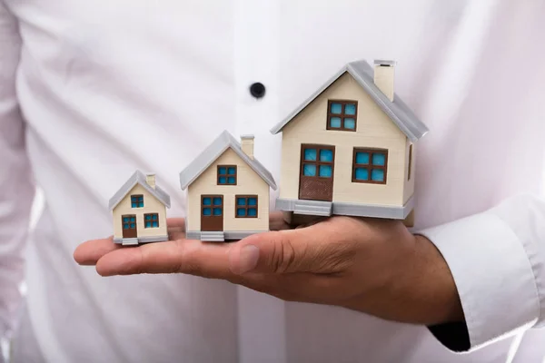 Close-up of a businessman\'s hand holding increasing size of house models