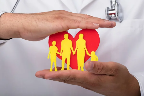 Mano Del Doctor Protegiendo Corazón Rojo Con Figuras Familiares Amarillas — Foto de Stock