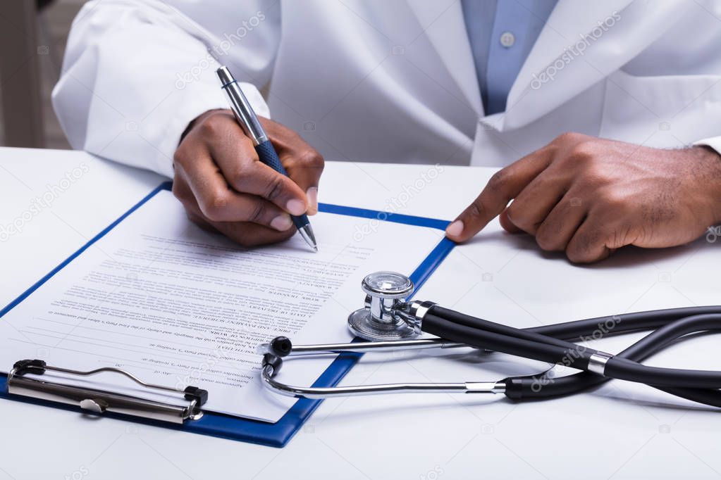 Stethoscope In Front Of Doctor Filling Form With Pen Over The Desk