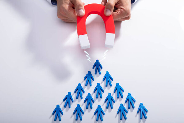 Businessman's Hand Attracting Blue Team With Horseshoe Magnet On White Background