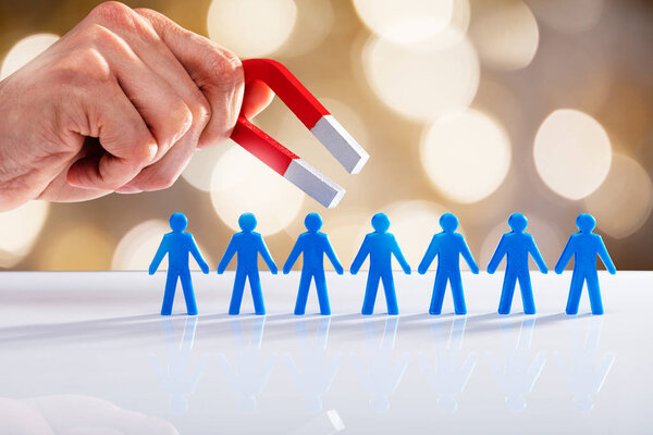 Рука человека, привлекающая синие человеческие фигуры с подковообразным магнитом на фоне Боке
