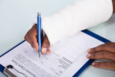 Panodaki sigorta hasar talep formu doldururken bandaj el ile yaralı adam havai görünümü