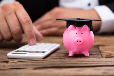 Business inessperson 's Hand Mezuniyet Şapkalı Piggybank' ın yanında Hesap Makinesi