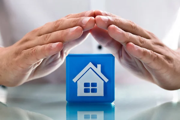 人的手的特写保护蓝色立方块与房子图标 — 图库照片
