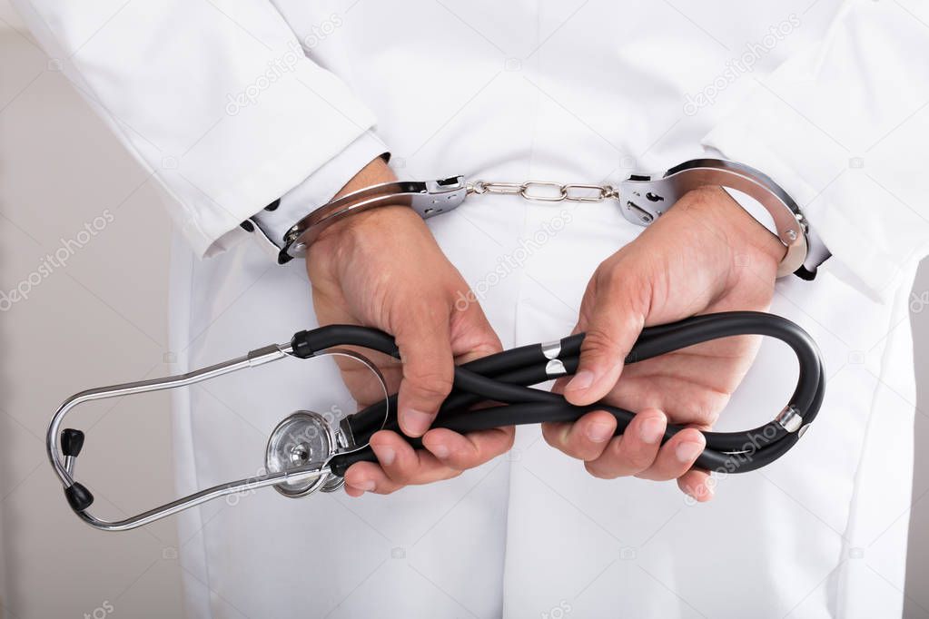 Doctor's hand with handcuff holding stethoscope behind