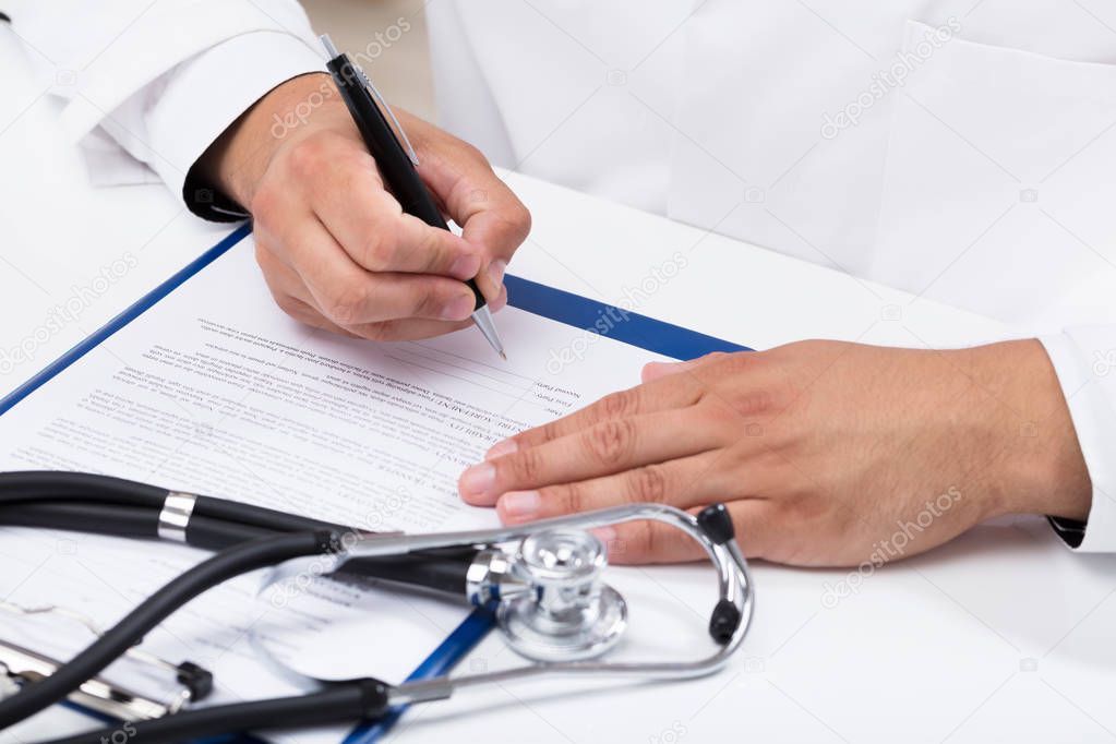 Doctor's hand signing document with stethoscope on desk