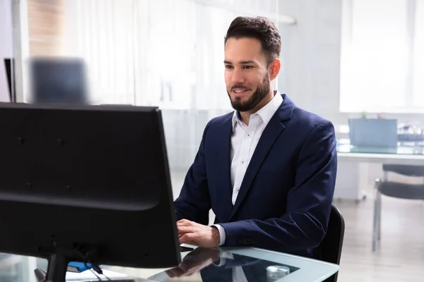 Smiling Young Businessman Using Computer In Office