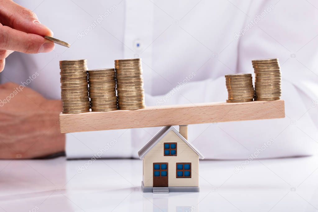 Businessman Stacking Coins On Seesaw Over House Model