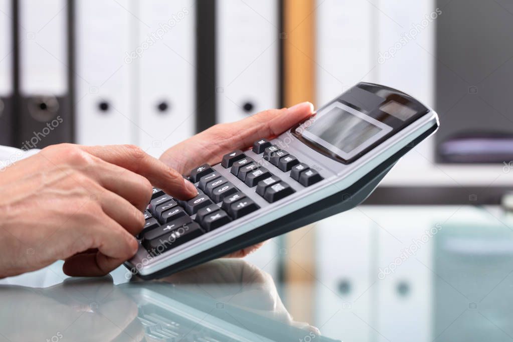 Businessperson's Hand Using Calculator Over Reflective Desk