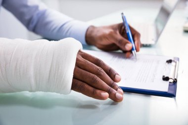 Panodaki sigorta hasar talep formu doldururken bandaj el ile yaralı adam havai görünümü