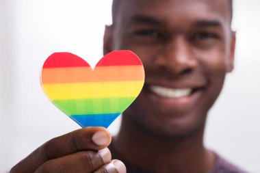 Smiling Man Holding Rainbow Heart In His Hand Against White Background clipart